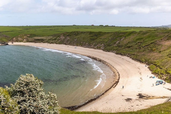 A coastal landscape with a sandy beach, grassy fields, and a clear view of the sea.