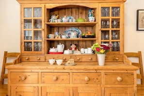 Un buffet en bois doté de portes en verre, dans lequel sont exposés divers ustensiles de cuisine, ainsi qu’un vase rempli de fleurs.