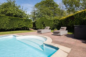 A swimming pool with a curved edge, surrounded by a patio area with two wicker lounge chairs.