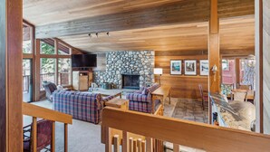 A spacious living area with a stone fireplace, wooden ceiling, and large windows.