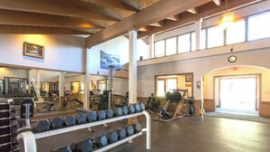 A gym with weightlifting equipment, mirrors, and a large window.
