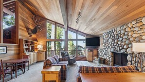 A cozy cabin interior with a stone fireplace, wooden furniture, and a large window overlooking the forest.