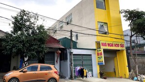Un edificio con fachada amarilla y blanca, un letrero que dice "NHÃ NHÃ HOA SÃU" y un coche naranja estacionado en la parte delantera.