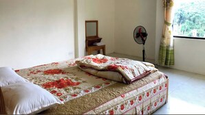 Un dormitorio con cama, mesita de noche, espejo, ventilador y ventana con cortinas.