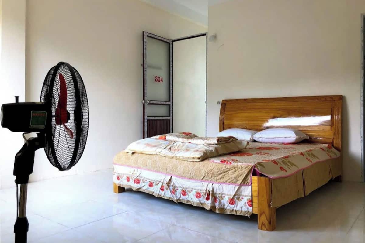 A bedroom with a bed, a standing fan, and a door with the number 304.