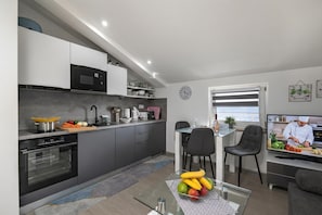 Une cuisine moderne dotée d’appareils électroménagers intégrés, un coin repas avec un téléviseur et une vue sur l’extérieur.