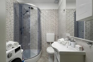 Un baño moderno con ducha envuelta en vidrio, inodoro y lavamanos con espejo.