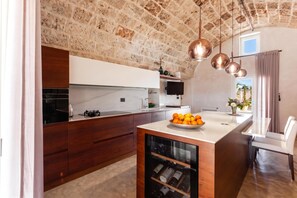 A modern kitchen with a stone wall, wooden cabinets, a built-in wine rack, and a dining area with a table and chairs.