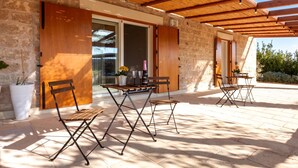 An outdoor patio with a wooden pergola, stone walls, and a table set for dining.