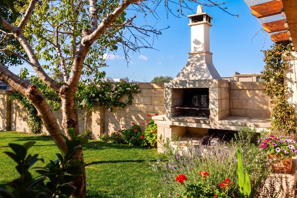 A garden with a stone wall, a tree, and a brick oven.