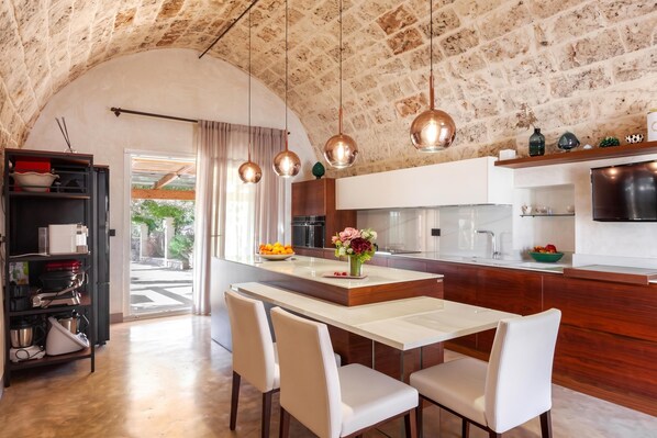 A modern kitchen with a central island, pendant lights, and a dining area with chairs.