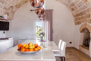 A dining area with a stone arch, a white table with a bowl of fruit, and a television on the wall.