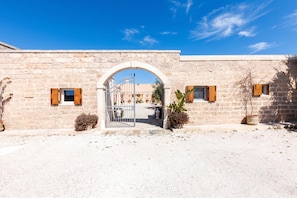 Un edificio in pietra con un arco centrale e un cancello in metallo. Ai lati dell'ingresso, vasi con piante.