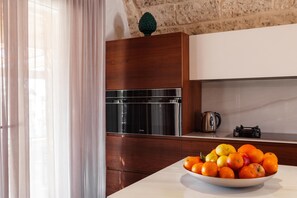 A modern kitchen with a built-in oven, a kettle, and a bowl of fruit on the counter.