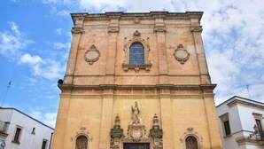 Un bâtiment historique doté d’une porte d’entrée centrale, flanquée de deux fenêtres en arc et d’une statue au-dessus de la porte.