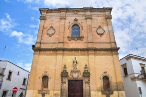 Un bâtiment historique doté d’une porte d’entrée centrale, flanquée de deux fenêtres en arc et d’une statue au-dessus de la porte.