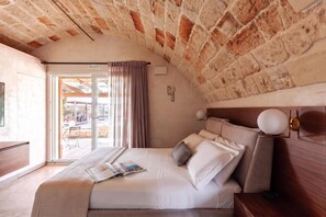 A bedroom with a brick ceiling, a bed with white bedding, a wooden nightstand, and a view of an outdoor patio.