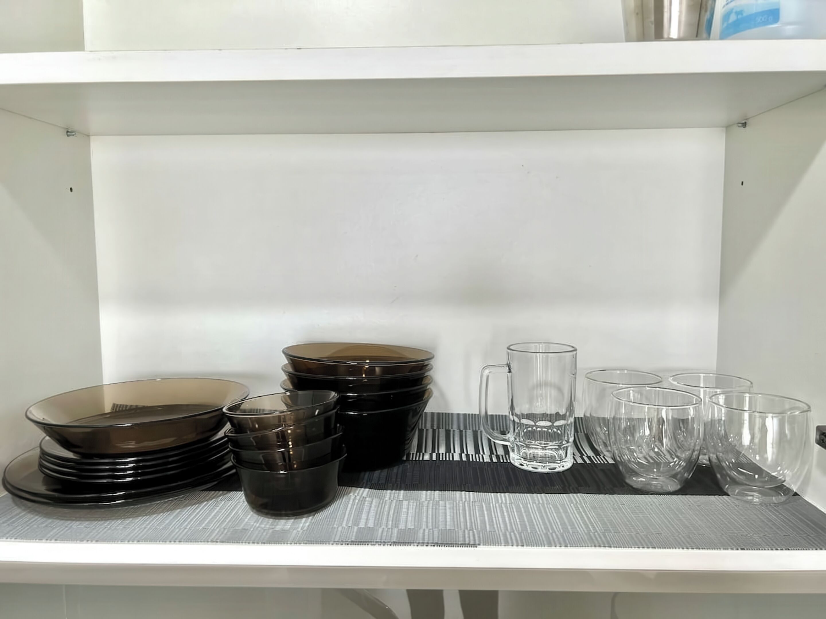 A white shelf with stacked black bowls and clear glasses.