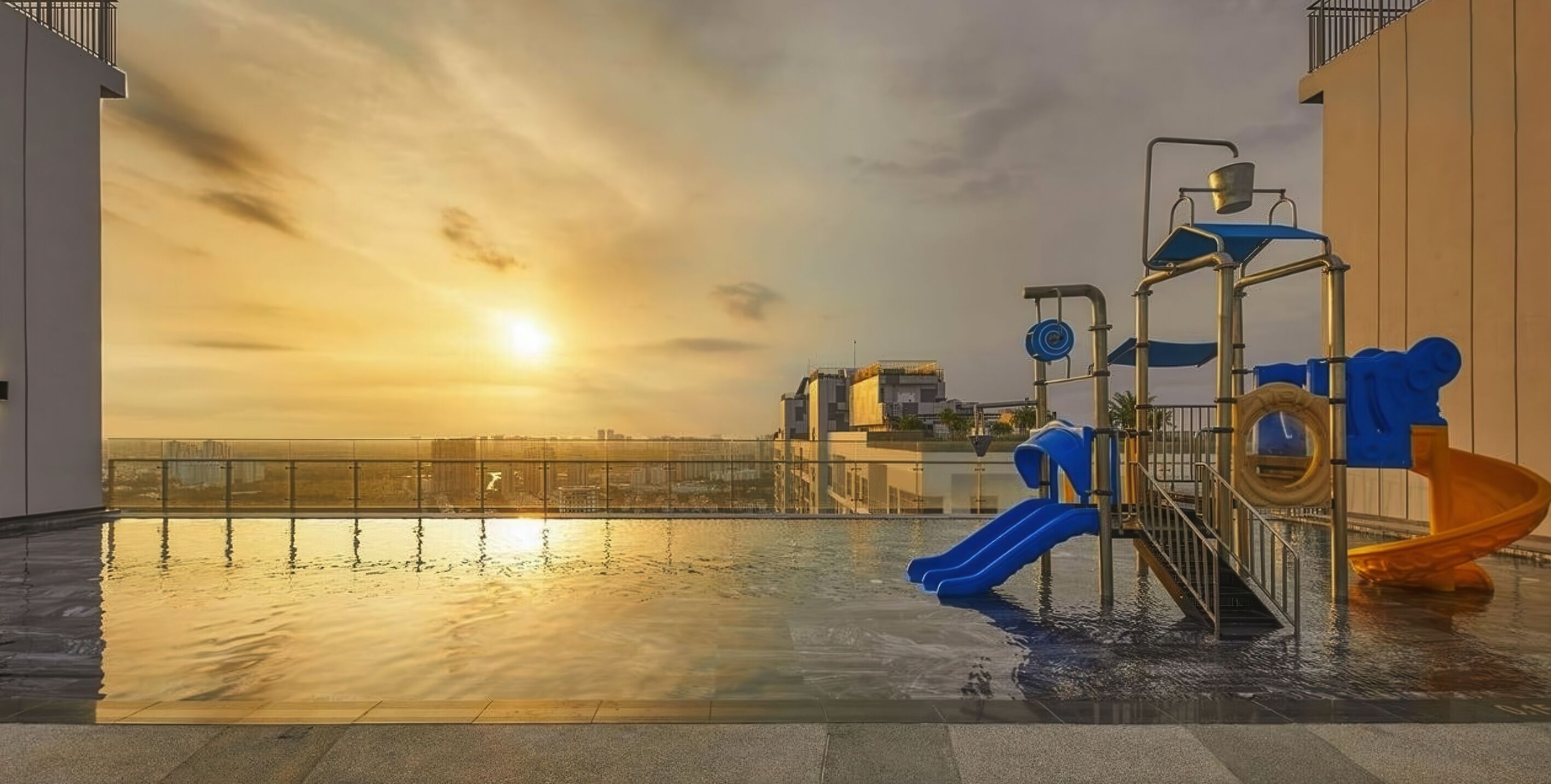 A rooftop pool area with a sunset view, a slide, and a water play structure.