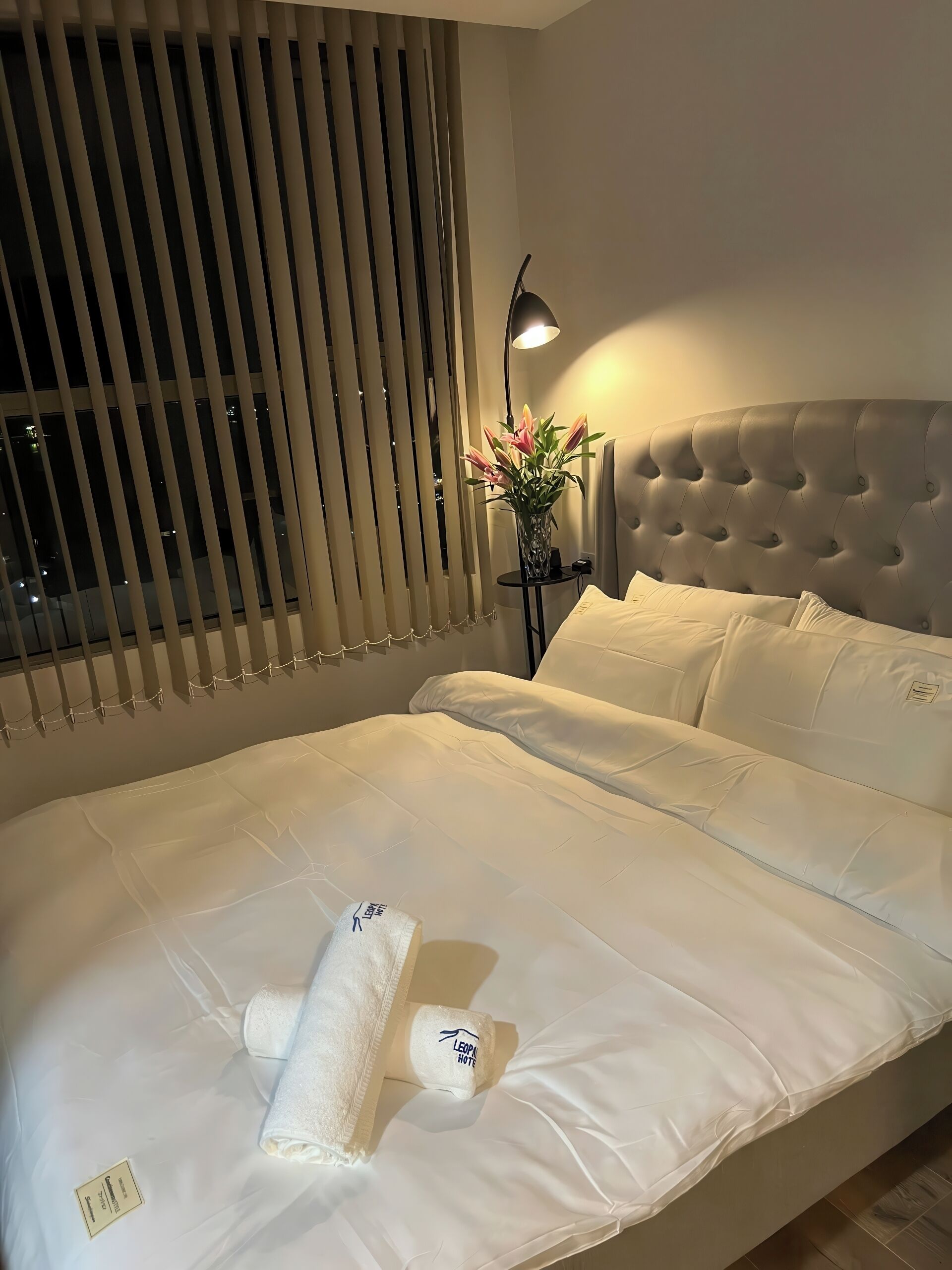 Un lit bien fait, avec du linge de lit blanc, une tête de lit et une lampe de chevet.
