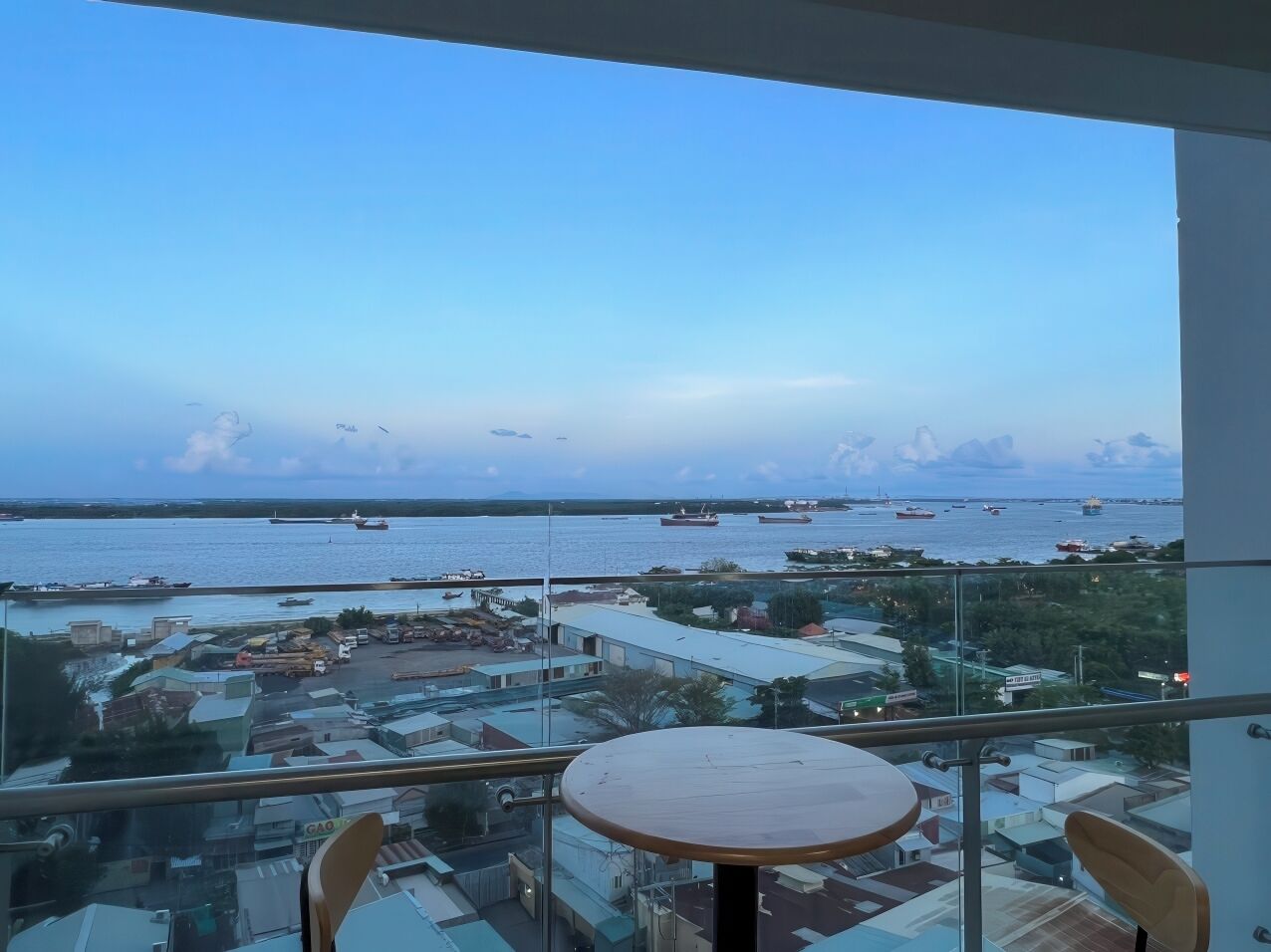 A balcony with a table and chairs, overlooking a marina with boats and buildings.