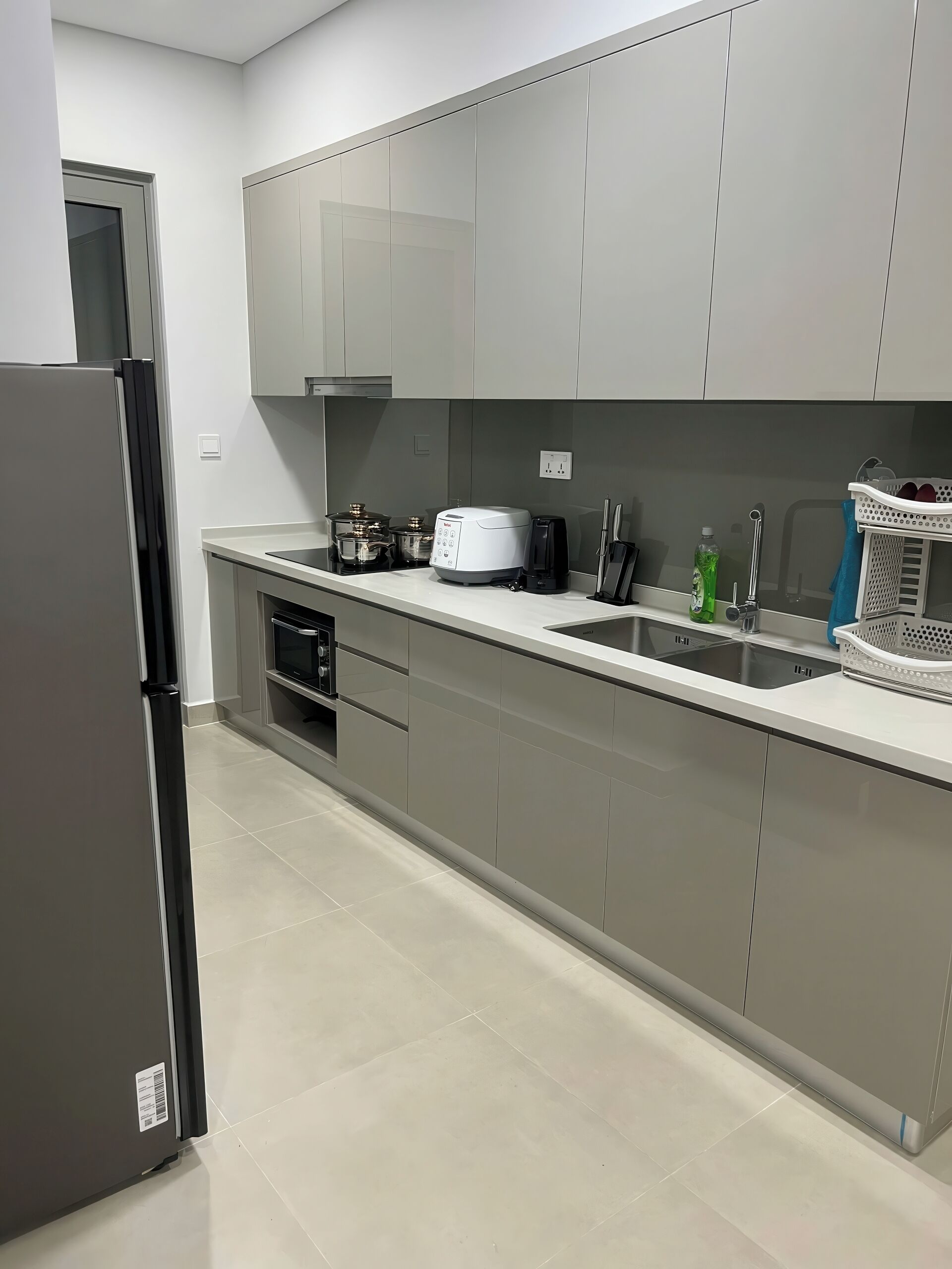 Una cocina moderna con gabinetes grises, un refrigerador de acero inoxidable, un horno empotrado, un lavamanos y una cafetera.