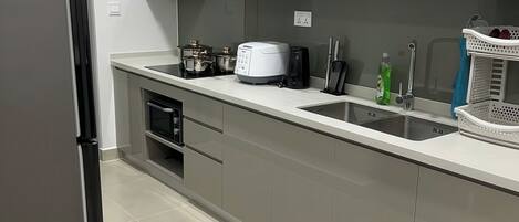Una cocina moderna con gabinetes grises, un refrigerador de acero inoxidable, un horno empotrado, un lavamanos y una cafetera.