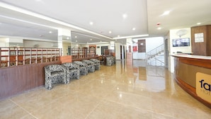 Un hall d’hôtel comprenant un comptoir d’accueil, un espace salon et un escalier menant aux étages supérieurs.