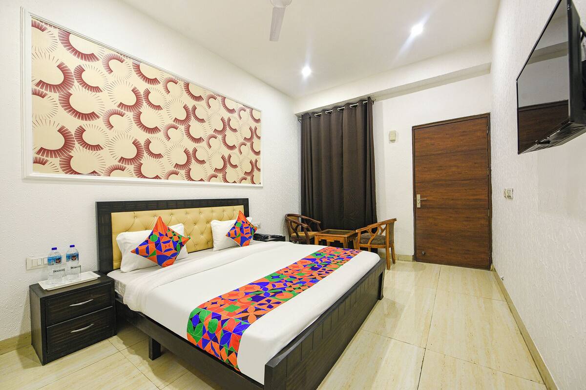 A hotel room with a bed, a nightstand, a chair, a wooden door, and a TV mounted on the wall.