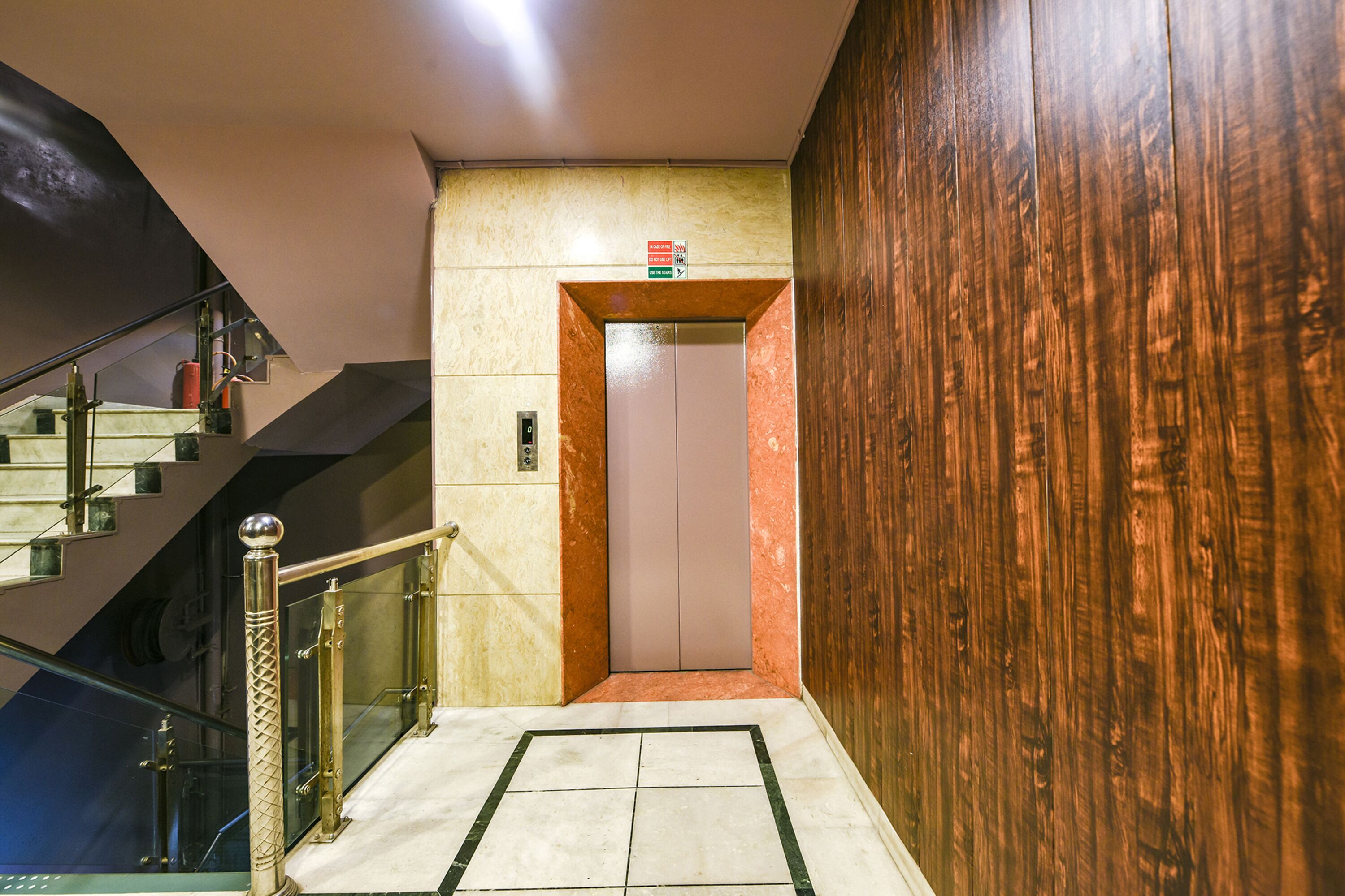 A modern elevator with a wooden panel wall and a glass railing beside a staircase.