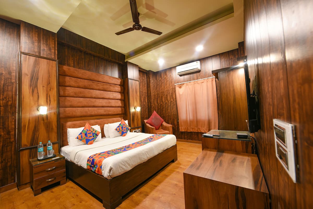 Une chambre d’hôtel avec un lit en bois, une table de chevet avec des bouteilles d’eau, un bureau et un ventilateur de plafond.