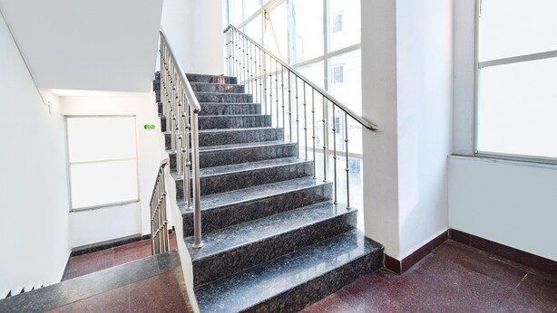 Eine Treppe mit Metallgeländern und Marmorstufen, die zu einem Zwischenpodest mit einer Tür führt.
