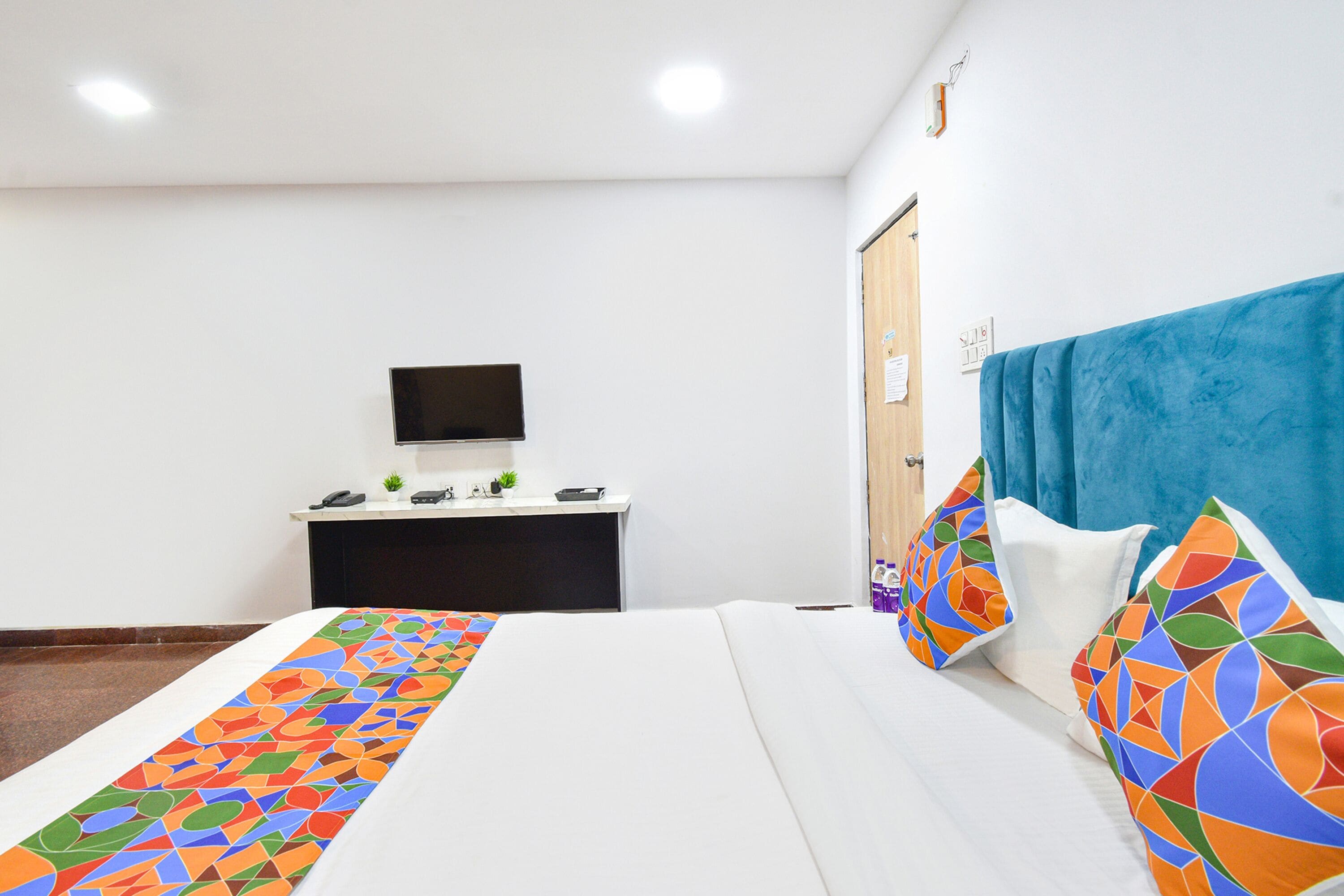 A hotel room with a bed, a desk with a computer, a TV, and a blue curtain.