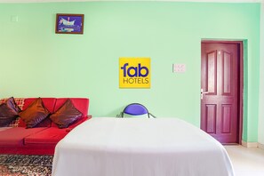 A hotel room with a bed, a red sofa with brown cushions, a chair, a door, and a sign for 'fab hotels'. - Fabhotel Bala Garden (Ootacamund)