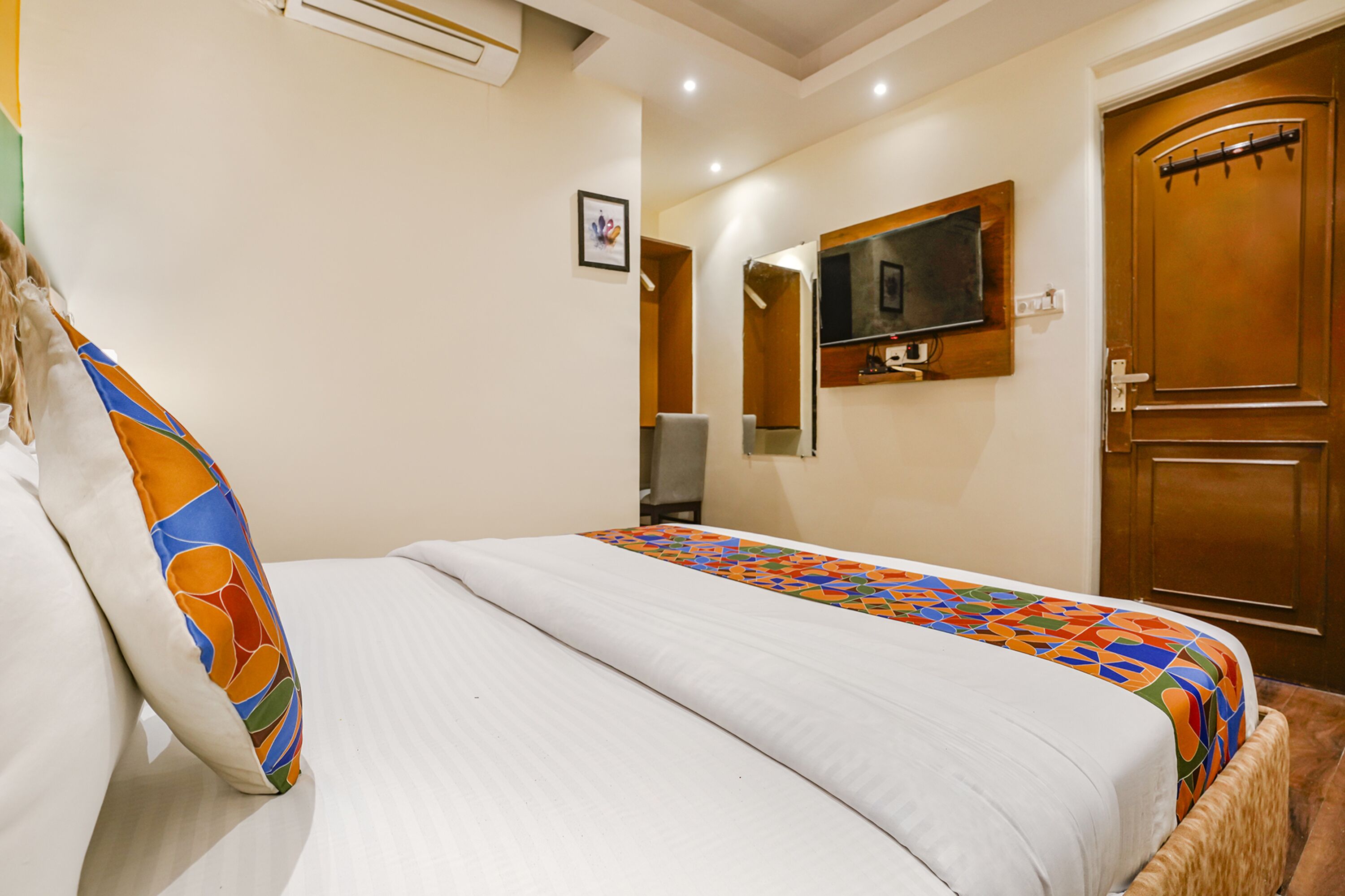 Een hotelkamer met een bed, een aan de muur bevestigde televisie en een houten deur.
