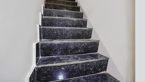 Un escalier avec des marches en marbre noir et des bords blancs, qui monte.