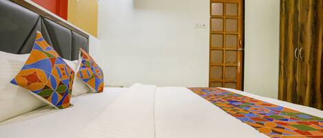A neatly made bed with a white comforter and colorful geometric pillows, a wooden wardrobe, and a door with frosted glass panels.