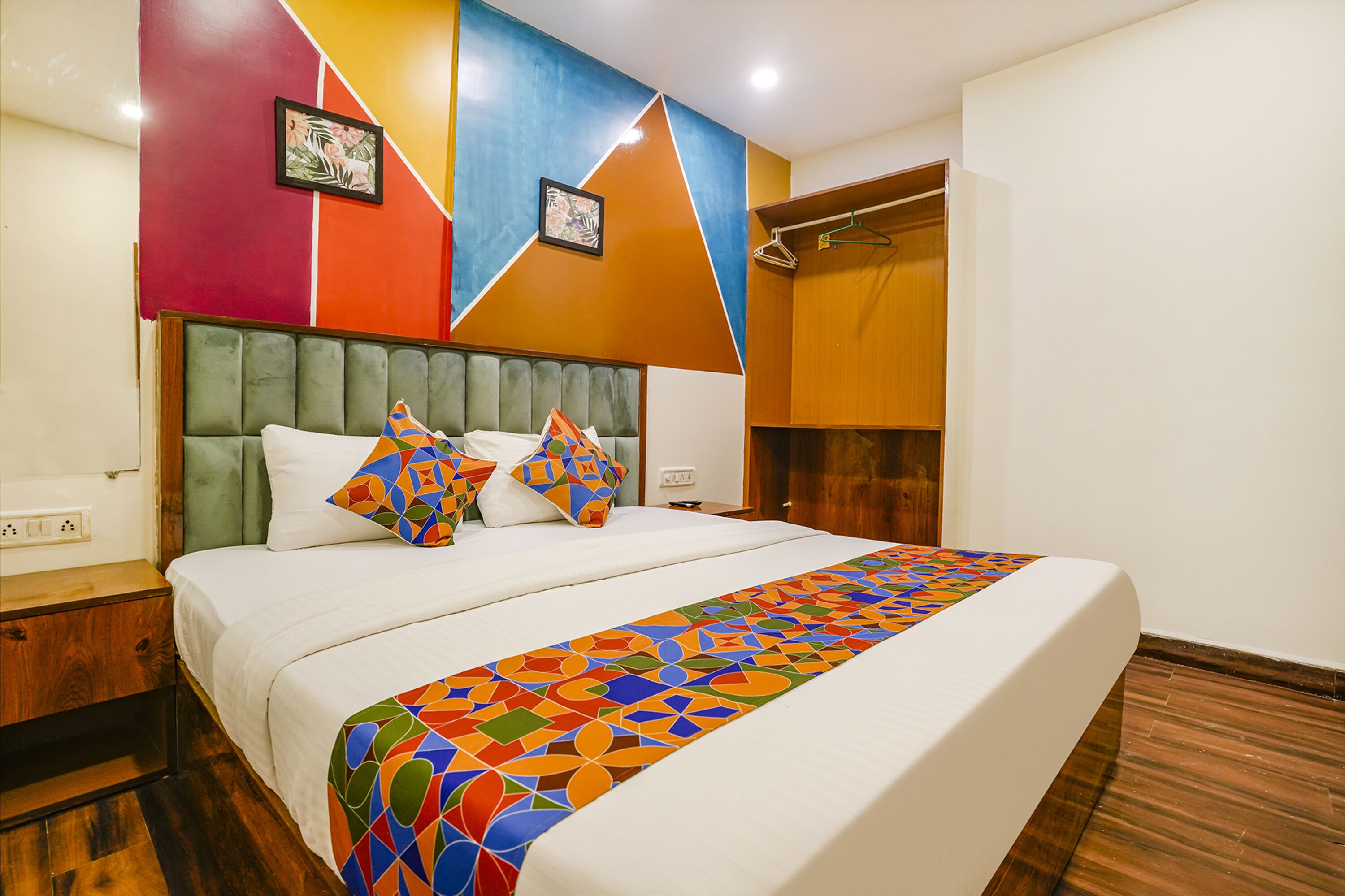 A neatly made bed with a colorful geometric-patterned bedspread and pillows, a wooden headboard, and a wall with a geometric design.