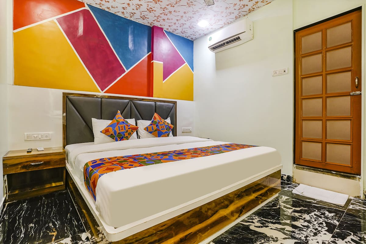 A hotel room with a bed, a nightstand, a wooden door, and a colorful geometric wall design.