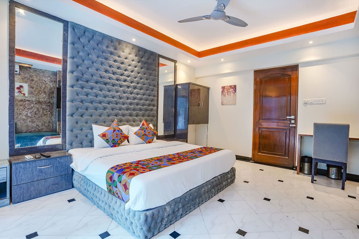 A modern bedroom with a large bed, a tufted headboard, a ceiling fan, and a wooden door.