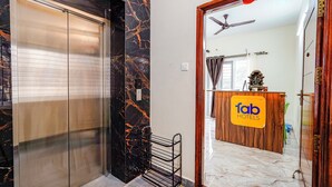 An elevator with a marble wall, a reception desk with a 'fab hotels' sign, and a ceiling fan. - Fabhotel Lucky Inn Grand Residency (Chennai)