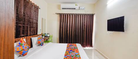 A hotel room with a bed, a desk, a chair, a TV, an air conditioning unit, and a ceiling fan.