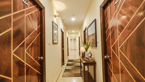A hotel hallway with wooden doors, a checkered rug, framed artwork, and a small table with a lamp and books. - Fabhotel Yogeshwara Grand (Hyderabad)