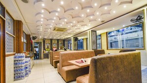 Um restaurante com bancos e mesas, piso ladrilhado e teto com iluminação embutida.