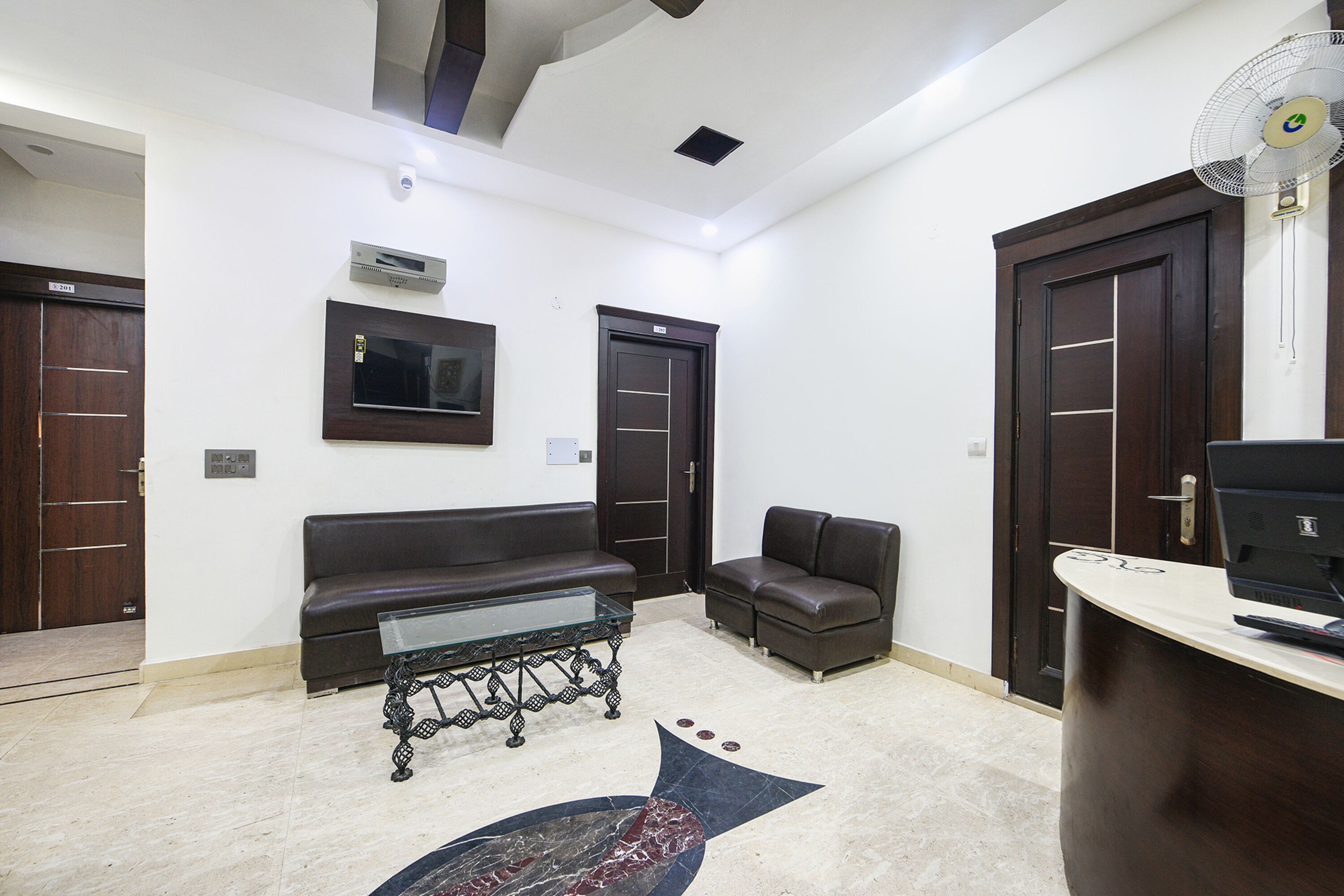 A modern waiting area with a leather sofa, a glass coffee table, and a desk with a computer.