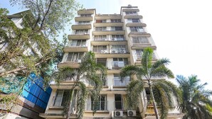 A multi-story residential building with balconies, air conditioning units, and surrounding palm trees. - Fabhotel Welcome Apartments (Mumbai)