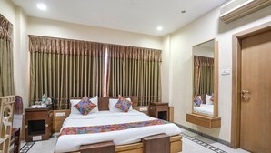 A hotel room with a large bed, wooden headboard, two bedside tables, a nightstand, a mirror, and a door. - Fabhotel Welcome Apartments (Mumbai)