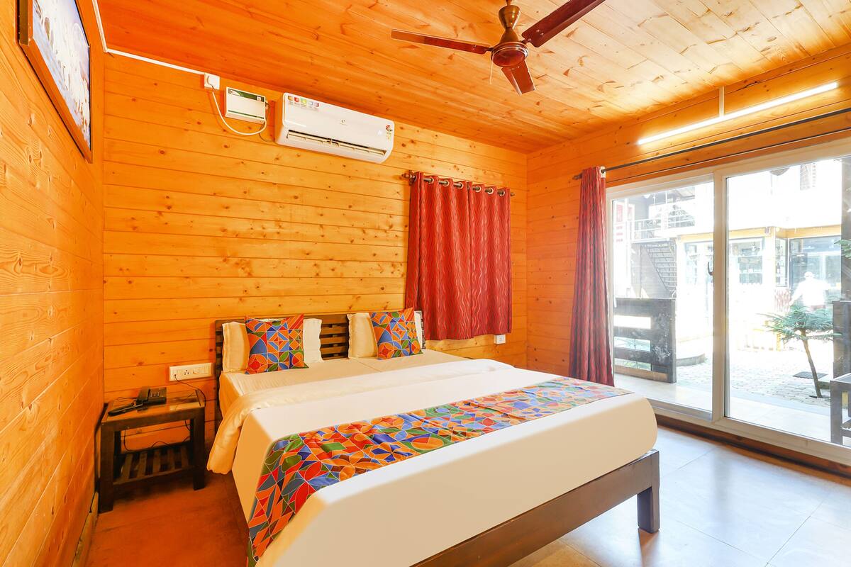Habitación de cabaña de madera con cama, ventilador de techo, aire acondicionado y vista a través de una puerta de cristal.