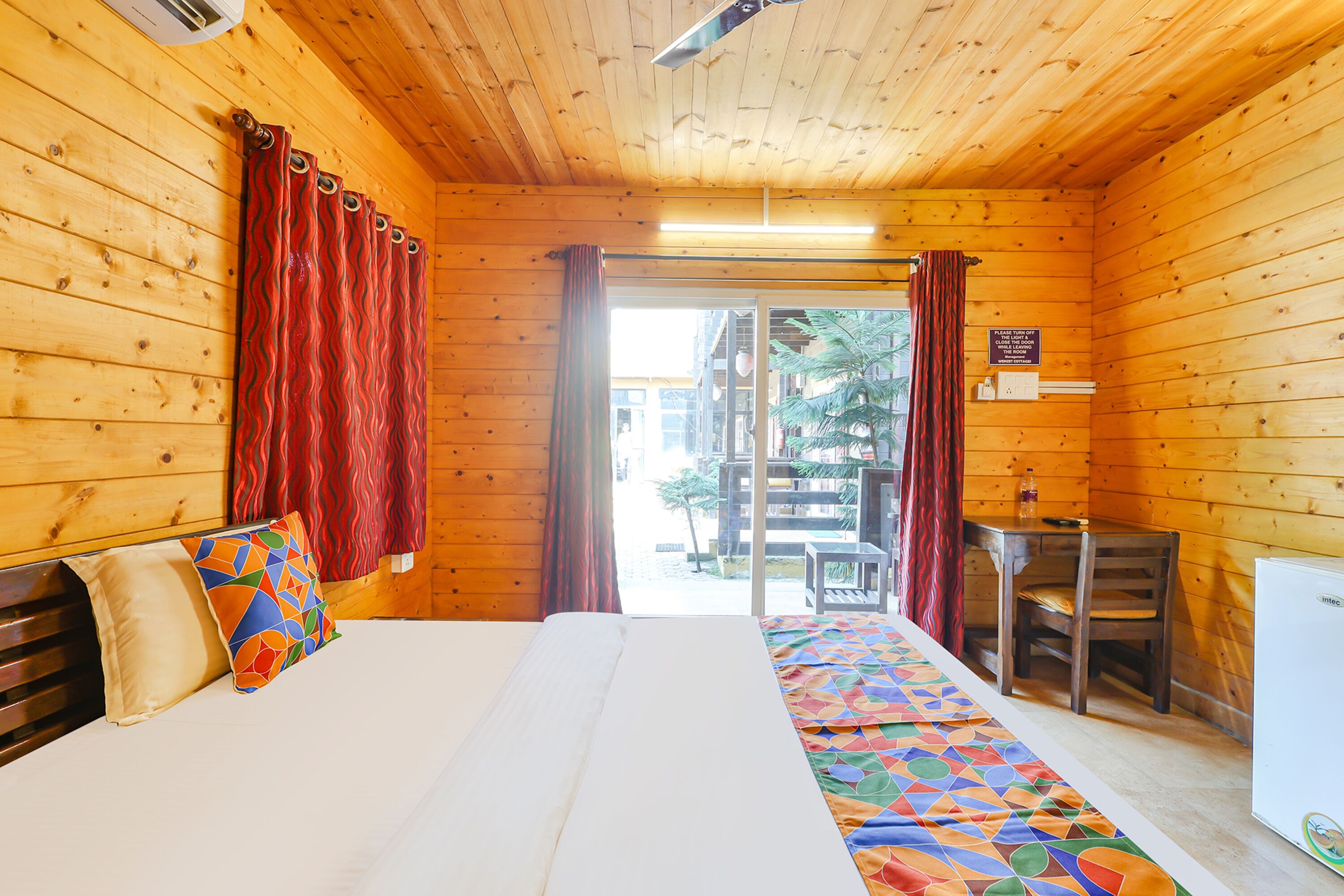 A wooden cabin room with a bed, a desk, and a chair.