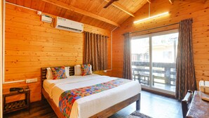 Un dormitorio tipo cabaña de madera con cama, ventilador de techo, aire acondicionado y un amplio ventanal con cortinas.